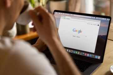 Mann trinkt aus einer Tasse Kaffee und schaut auf seinen Bildschirm. Dort ist Google in einem Browser geöffnet.